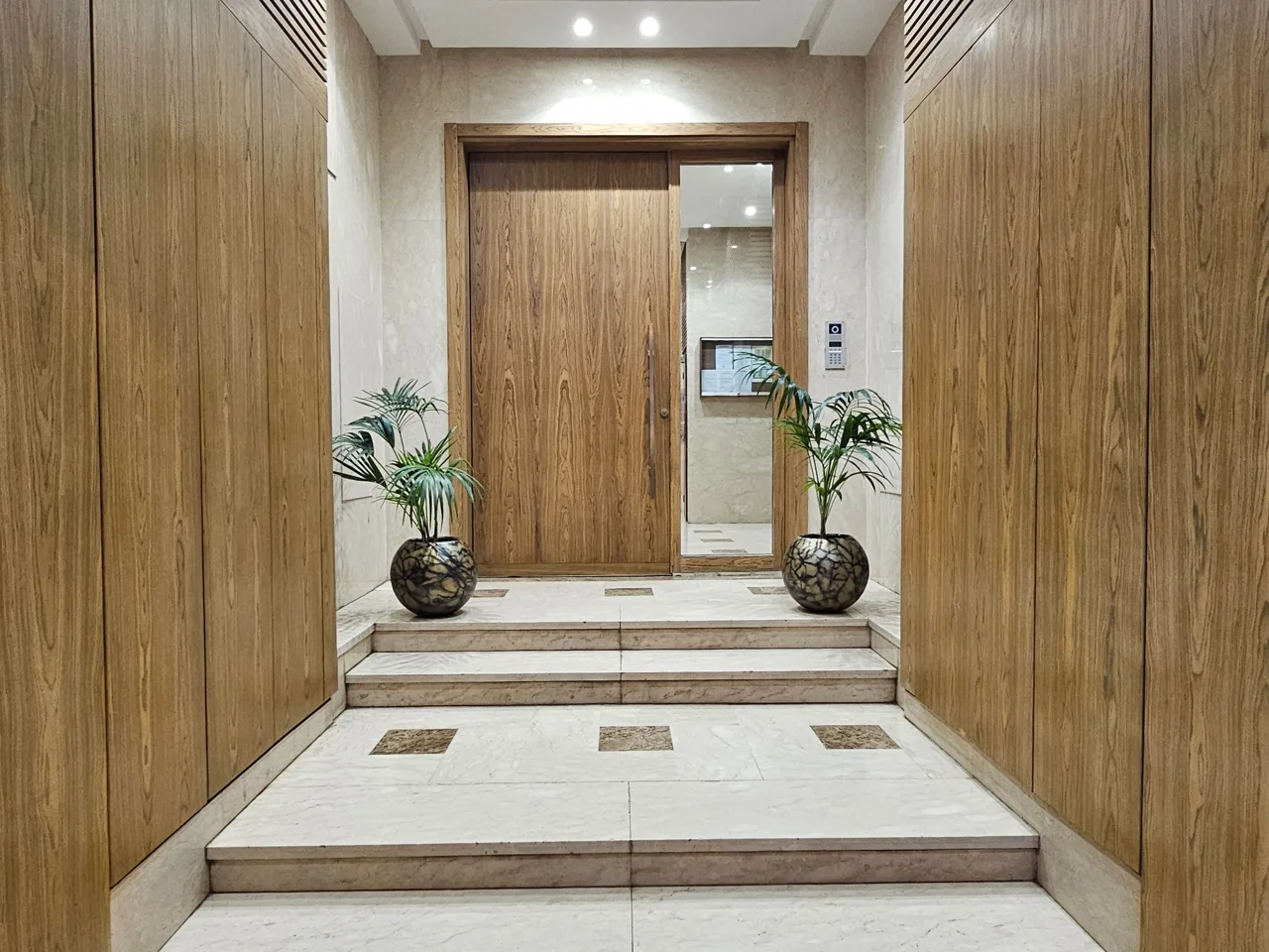 Entrée de la Résidence Jacinth, avec porte en bois, sol en marbre et plantes